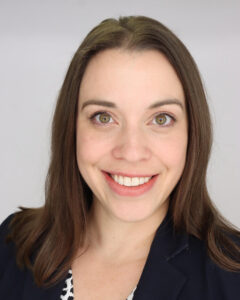 Dr. Allison E. Garda, M.D., radiation oncologist at Mayo Clinic, stands against a light-colored wall wearing a dark button-up shirt and glasses. She smiles warmly and wears a pendant necklace, conveying professionalism and approachability.